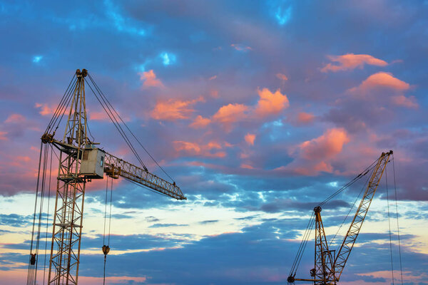 Tower cranes against the sky with clouds at sunset.