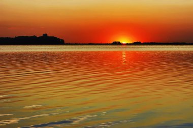 Gölün üzerinde gün batımı - güneş ve gökyüzü suya yansıyor.