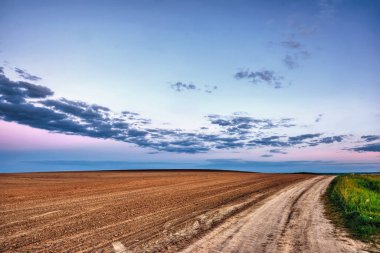 Akşam kırsal manzarası - gün batımında bulutlu mavi gökyüzü tarlalar ve toprak yol üzerinde.