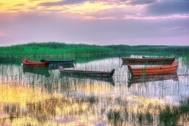 Gölün üzerinde akşam - suda ahşap kayıklar ve gün batımında sazlıklar.