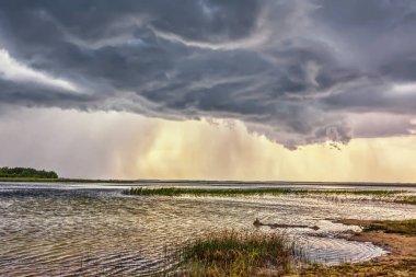 Gölün üzerinde fırtına bulutları ve çimen ve ağaçlarla kıyı şeridi.