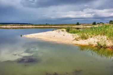 Nehrin tepe kıyıları üzerinde ağaçlar ve çalılarla kaplı güzel fırtına bulutları durgun suya yansıyor..