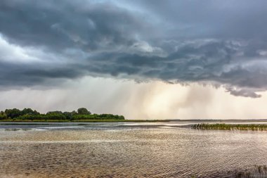Göl üzerinde fırtına ve gün batımında kıyı şeridi.