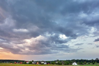 Gün batımında orman ile köyün üzerinde fırtına bulutları.