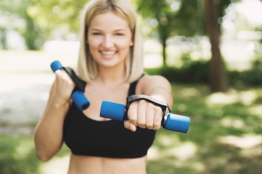 Genç kadın parkta dumbbells ile eğitim
