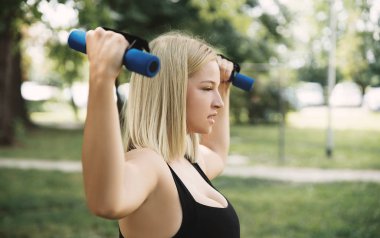 Genç kadın parkta dumbbells ile eğitim