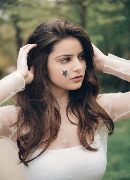 Young brunette woman in mesh shirt with stars on her face