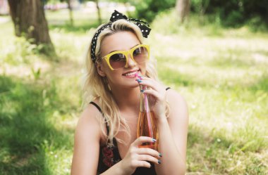 Güneş gözlüklü, içki şişeli genç bir kadın.