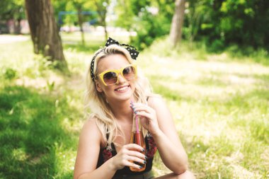 Parkta içki içen güneş gözlüklü genç kadın.