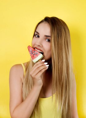 Sarı arka planda dondurmayla poz veren genç bir kadın.