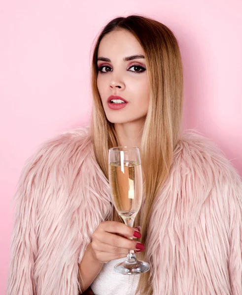 Young woman in pink fur coat holding glass of champagne