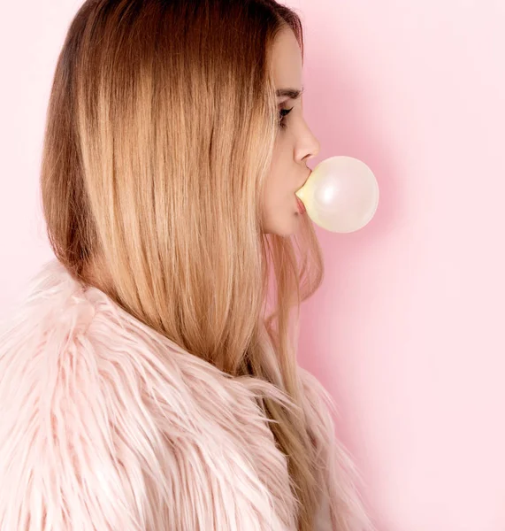 Young woman in pink fur coat with bubblegum