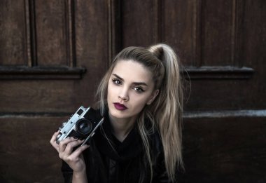 Genç, güzel bir kadın elinde eski model bir kamera tutuyor. 