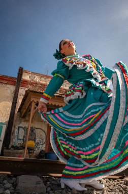 Turkuaz giyinmiş, gökkuşağı kurdeleli Meksikalı bir folklorik dansçının sanatsal çekimi.,