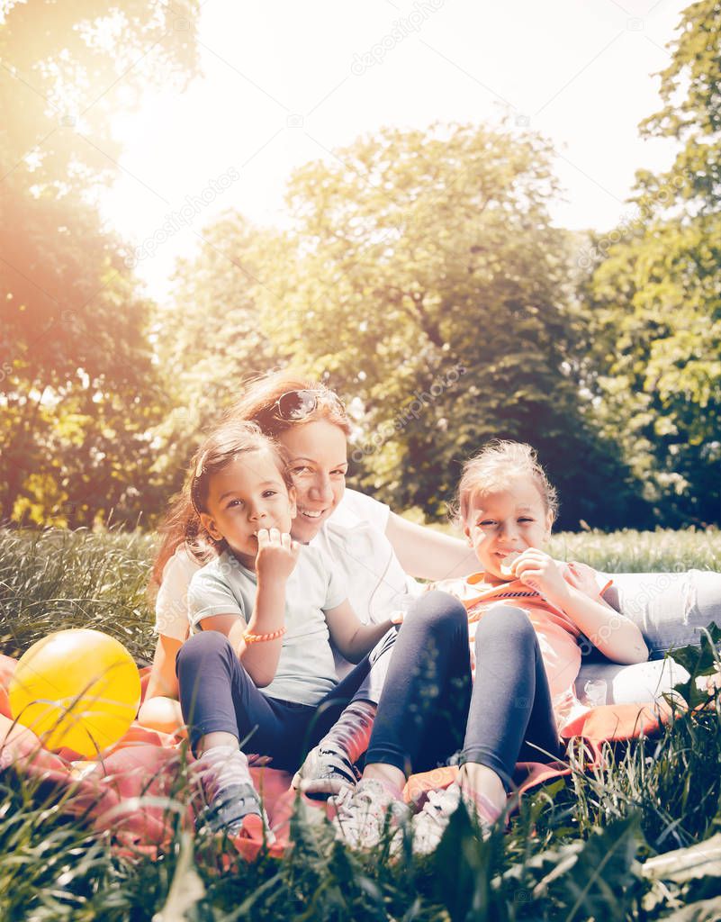 Mother and daughters in the park. They sit on the grass, laugh and enjoy their free time.