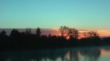 Sunrise orman arkasında. Yansıma gölde. Masmavi gökyüzü.