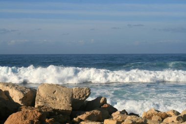 Beyaz köpüklü dalgalar üzerinde bir kayalık sahil, Akdeniz'in bir yaz akşamı