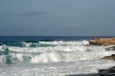Beyaz köpüklü dalgalar üzerinde bir kayalık sahil, Akdeniz'in bir yaz akşamı