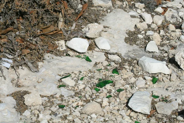 Green glass shards lying among stones on Limassol coastline