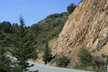 İki şeritli asfalt boş bir yol, büyük kahverengi taş, yeşil tepeler ve mavi gökyüzü güneşli bahar gününde Kıbrıs Troodos Dağları'nda