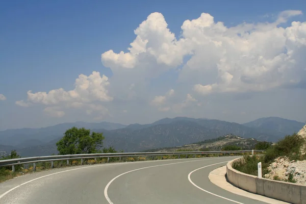 Panoramik dağ silsilesi ve mavi gökyüzü güneşli bahar gününde Kıbrıs Troodos Dağları ile iki şeritli boş yol asfalt eğrisi