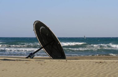 Bulutsuz mavi gökyüzü ve denizin dalgalı önünde boş bir kumlu plaj yan yatan ip güneş şemsiyesi