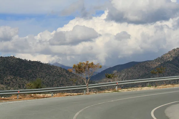 Curve of two lane asphalt road in the Troodos mountains, Cyprus with a panoramic view of the mountain range and the clouds in the sky on a nice winter day
