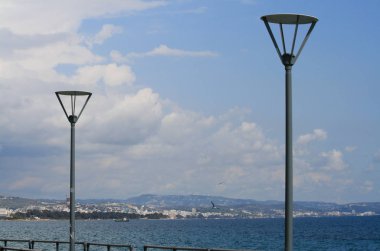 Mavi deniz, gökyüzü beyaz bulutlar ile ve bir görünüm bir kıyı şeridi önünde rıhtımda iki metal sokak lambaları