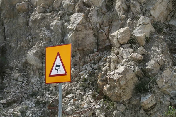 Close-up of a slippery road warning sign in front of a white rocky cliff