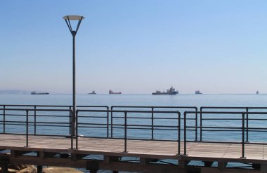 Güneşli bir günde mavi gökyüzünün önünde metal korkulukları ve sokak lambası ile boş sahil yolu