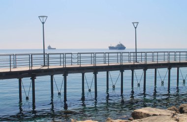 Güneşli bir günde mavi gökyüzünün önünde metal korkulukları ve sokak ışıkları ile Limasol Molos kordonunda boş sahil yolu