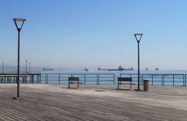 Güneşli bir günde bir ahşap iskelede bir deniz manzaralı ve sokak lambaları ile boş banklar