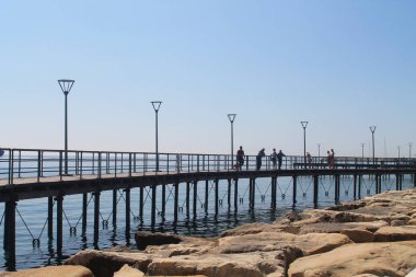 Limasol, Kıbrıs, 22 Mart, 2019: yürüyüş ve ayakta insanlarla güneşli bir günde Molos kordonunda metal korkuluk ve sokak lambaları ile Seaside yolu