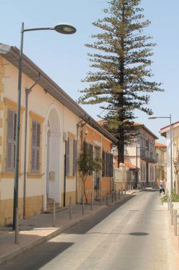 Limasol, Kıbrıs, 24 Nisan 2019: Güneşli bir günde geleneksel Akdeniz tarzı binalar, bir yaya ve uzun bir sedir ağacı ile Eski şehir dar sokak
