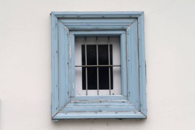 Beyaz bir duvarda metall ızgara ile küçük bir mavi ahşap pencere yakın çekim