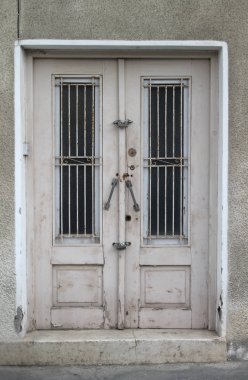 Gri taştan bir duvarda metal ızgaraları olan iki yapraklı beyaz ahşap bir ön kapı.