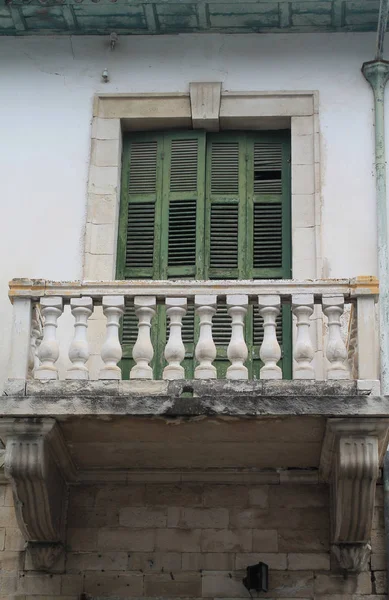 Close-up of a shabby old balcony with the white stone pillars and the green wooden shutters