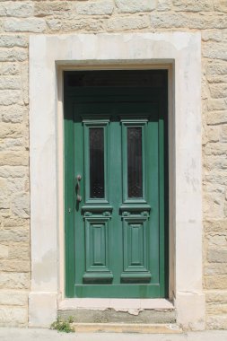 Güneşli bir günde beyaz bir taş duvarda iki cam paneller ile yeşil ahşap ön kapı
