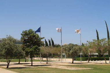 Lefkoşa, Kıbrıs, 7 Mayıs 2019: Güneşli bir günde Kıbrıs Üniversitesi Kampüsü'ndeki çimenlikte üç bayrak direğinin üzerinde Avrupa bayrağı, Kıbrıs Üniversitesi bayrağı ve Kıbrıs ulusal bayrağı