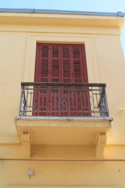 Metal ızgaraları ve kapalı kahverengi ahşap panjurlu bir pencere ile retro tarzı balkon ile sarı bir ev duvarının bir parçası 