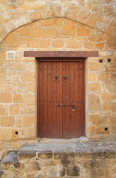 Old-fashioned brown wooden outside door with two metal knockers and a lock in an old stone wall 
