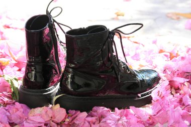 Güneş ışığında kuru pembe begonviller yaprakları arasında siyah patent deri parlak çizmeler bir çift yakın çekim