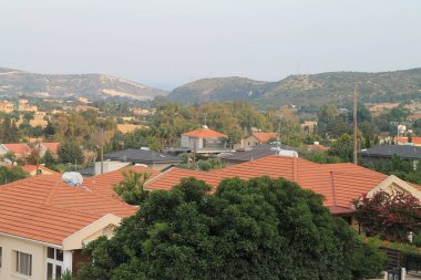 Akdeniz köyünün kahverengi kiremitli çatılarının, yeşil ağaçların, dağların ve gökyüzünün alacakaranlıkta panoramik görünümü