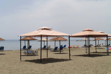 Güneşli bir günde şezlong, şemsiyeler ve gazebos ile kumlu plaj