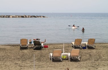 Şezlong, Kano ve güneşli bir günde üç tanınmayan kişi ile kumlu plaj