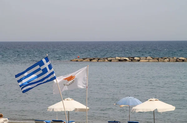 National flags of Cyprus and Greece waving over a Limassol  beach in front of the Mediterranean sea on a sunny day