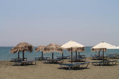 Güneşli bir yaz gününde Akdeniz ve berrak mavi gökyüzü önünde boş şezlong ve tte saman ve tuval şemsiye ile Kumlu plaj