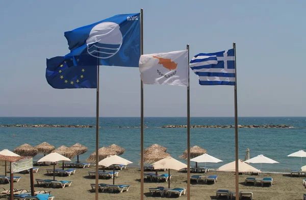 The Blue Flag, the European flag and the national flags of Cyprus and Greece waving over a Limassol  beach in front of the clear blue sky and the Mediterranean sea on a sunny summer day