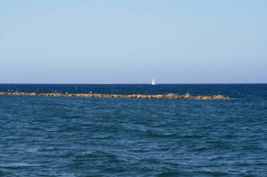 Ufukta beyaz bir yelkenli tekne ve Limasol sahilinden açık mavi gökyüzü ile lacivert denizin panoramik manzarası 