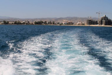 Koyu mavi denizde Limasol şehri ve dağları olan bir yelkenliden beyaz köpüklü dalgalar.
